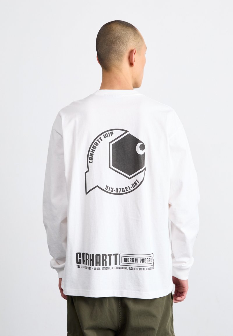 Hvit skjorte med lange ermer som har et svart grafisk fiskedesign og tekst på baksiden, med ribbede mansjetter og rett kant.