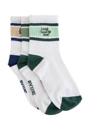 Trois paires de chaussettes blanches courtes avec des accents colorés sur les orteils et les talons, ainsi que des rayures près du bord-côte, avec le texte de la marque sur chaque paire.