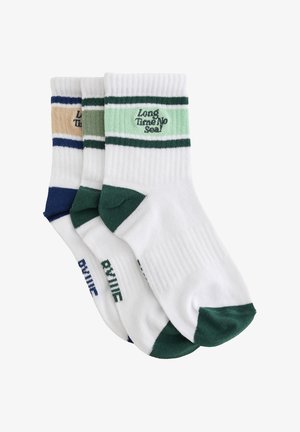 Trois paires de chaussettes blanches courtes avec des accents colorés sur les orteils et les talons, ainsi que des rayures près du bord-côte, avec le texte de la marque sur chaque paire.