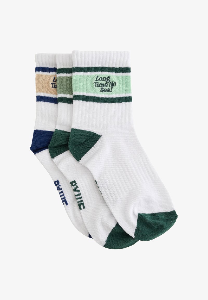 Trois paires de chaussettes blanches courtes avec des accents colorés sur les orteils et les talons, ainsi que des rayures près du bord-côte, avec le texte de la marque sur chaque paire.