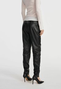Czarne skórzane spodnie o luźnym kroju, z charakterystycznymi detalami szwów. W zestawieniu z czarnymi szpilkami, które podkreślają projekt dołu.