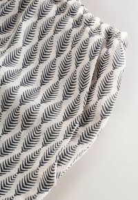 Weißer Stoff mit schwarzem Farnmuster; verfügt über einen gerafften Taillenbund und eine weiche, strukturierte Oberfläche; entworfen für Komfort und Atmungsaktivität.