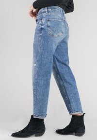 Vaqueros de mezclilla azul claro con un corte holgado, detalles desgastados, piernas rectas y cintura alta, combinados con botines negros al tobillo.