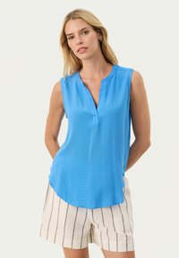 Top blu senza maniche con scollatura a V e orlo curvo, realizzato in tessuto liscio. Abbinato a pantaloni corti a righe chiare.