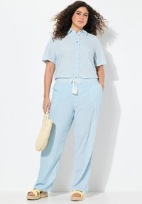 Camicia a maniche corte a righe blu chiaro con bottoni abbinata a pantaloni larghi coordinati. Presenta una vita con coulisse e una borsa di paglia.