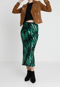 Chaqueta de motorista de ante marrón sobre una camiseta negra corta, combinada con una falda midi verde con rayas de tigre negras y botas negras hasta el tobillo.