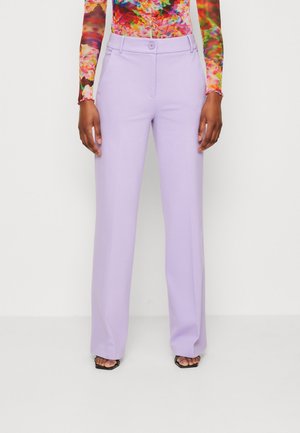 Fiołkowe, szerokie spodnie z gładką fakturą, dwoma przednimi kieszeniami i pojedynczym zapięciem na guzik. Połączone z kolorową bluzką z długim rękawem.