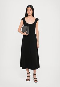 Zwart midi-jurkje met cap sleeves, aansluitende lijfje en uitlopende rok. Gepaard met een slanke zwarte clutch en strappy zwarte hoge hakken.