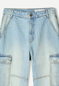 Svijetloplave traper cargo hlače s očnim džepovima, zatvaranjem na patentni zatvarač i kontrastnim šavovima. Tekstura izgleda glatko s izblijedjelim finišem.