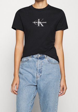Black Calvin Klein Jeans t-shirt worn with high-waisted light blue denim jeans, showing torso and arms of a standing person.