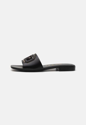 Black flat slide sandals with a wide strap featuring a decorative gold-accented buckle, made from smooth leather with a low heel.