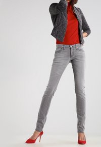 Szare dżinsy typu skinny z pięcioma kieszeniami, w połączeniu z czerwoną bluzką i teksturowaną czarną kurtką bomber. Dodatki to czerwone buty na obcasie.