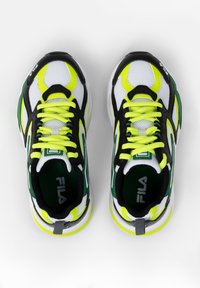Vita mesh-sneakers med svarta och gröna detaljer, ljusa gula snören och dekorationer, tjock sula, Fila-logotyp på tungan och hälen.