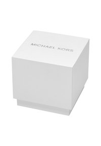 Caja de cartón blanco texturizado con un acabado suave. La parte superior presenta "MICHAEL KORS" en impresión plateada. Forma cuadrada con una base a juego.