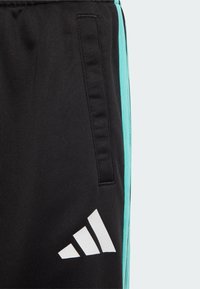 Mustat urheiluhousut, joissa on turkoosi raita sivussa, teksturoitu kangas ja valkoinen Adidas-logo alhaalla jalassa.