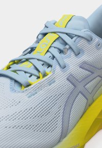 Ανοιχτό μπλε αθλητικό παπούτσι με λογοτυπο Asics σε λεβάντα, κίτρινη ετικέτα στη γλώσσα και ανοιχτό κίτρινο σόλα, με λεπτομερή κορδόνια και υφή από δίχτυ.