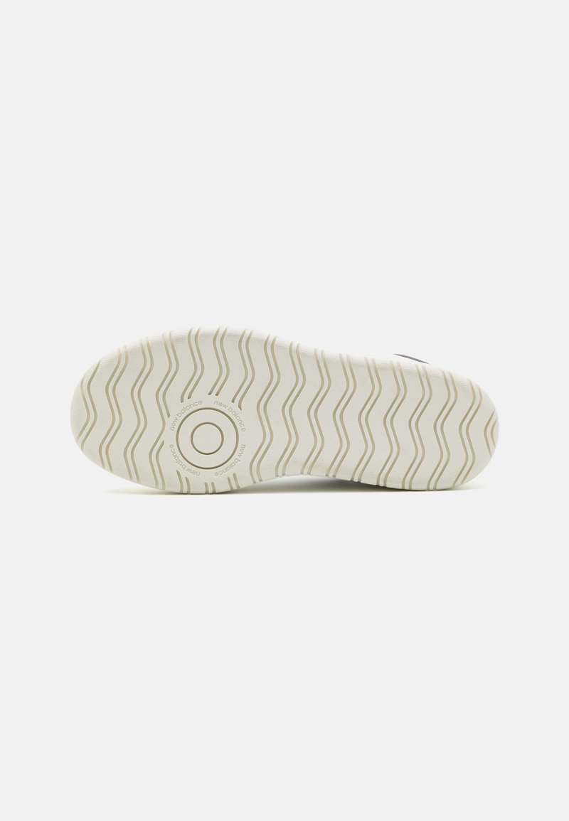 Semelle de chaussure, matériau en caoutchouc, blanche avec un motif de semelle ondulé, logo circulaire au centre, texture lisse, couleur neutre.
