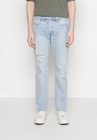 Light blue denim jeans with distressed details, straight leg cut, five-pocket design, and belt loops, paired with white sneakers and a green shirt.