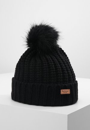 Bonnet noir en tricot épais avec un gros pompon duveteux sur le dessus et une petite étiquette en cuir marron portant l'inscription « Barbour England » sur le revers.