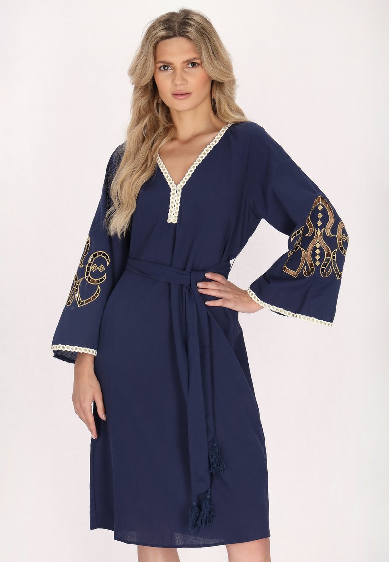Rochie de navy cu decolteu în V, mâneci largi decorate cu broderie aurie complicată și un cordon în talie cu ciucuri. Textură ușoară a materialului.