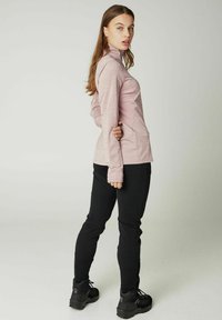 Hellrosa Langarmshirt mit hohem Kragen, kombiniert mit schwarzen, taillierten Hosen und schwarzen Sportschuhen. Glatter Stoff mit feiner Textur.