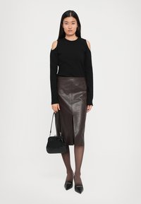 Black long-sleeve top with cut-out shoulders, brown leather pencil skirt, black handbag, sheer tights, and pointed black heels.