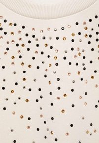 Felpa color crema con superficie testurizzata decorata con paillettes nere, dorate, argentate e rosa dorato di diverse dimensioni disposte in modo casuale.
