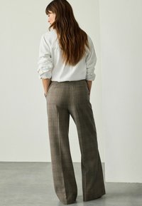 Plaid trousers in brown and gray tones, featuring a high waist, wide leg, and side pockets; made from woven fabric with a smooth texture.