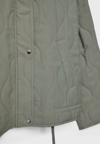 Gestepptes Jacket aus olivgrünem Stoff mit wellenförmiger Textur, Druckknopfverschluss und einer seitlichen Tasche mit flachem Design.