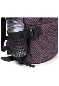 Fialový batoh s diagonálním vzorem kosočtverců, vybavený boční síťovanou kapsou na láhev s vodou a nastavitelnými černými popruhy.