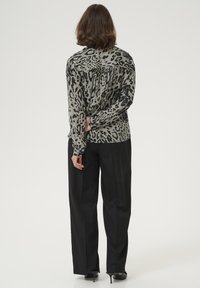 Blusa in stampa leopardata grigia e nera, caratterizzata da una vestibilità comoda, maniche lunghe e pieghe sul retro. Abbinata a pantaloni neri.
