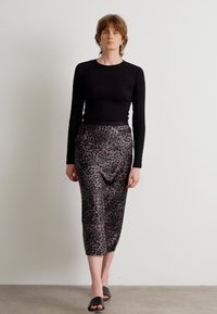 Svart langermet topp i kombinasjon med en midtlengde leopardmønstrete skjørt i grått og svart. Modellen har på seg svarte slip-on sko.