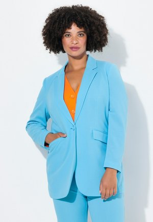 Helleblaue Blazer mit Taillenschnitt, Reverskragen und Vordertaschen, kombiniert mit einer orangefarbenen Knopfbluse. Glatte Textur, minimale Details.