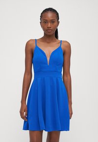 Blue sleeveless dress with a deep V-neck, fitted bodice, and flared skirt. Smooth fabric, minimalist design, and adjustable straps.