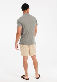 Grijze poloshirt met korte mouwen, gecombineerd met lichtbeige corduroy shorts die een gestructureerde afwerking en een ontspannen pasvorm hebben. Bruine sandalen maken de look af.