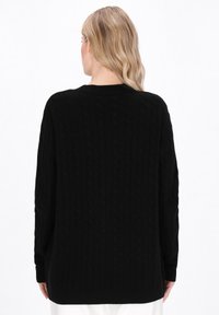 Maglione nero a maglia con scollo rotondo, maniche lunghe e polsini a coste. Il motivo testurizzato aggiunge dimensione all'indumento.