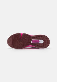 Semelle d'une chaussure de sport rose avec une bande de roulement marron texturée et un motif de rainures courbes sur un fond blanc propre.
