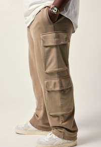 Beige cargobroeken gemaakt van zachte stof, met twee grote zijzakken, een relaxed fit en een geribbelde textuur. Gecombineerd met witte sneakers.
