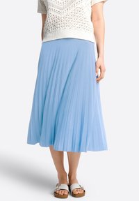 Gonna plissettata azzurro chiaro con una vestibilità morbida, realizzata in tessuto soffice, abbinata a sandali bianchi con dettagli a fibbia.