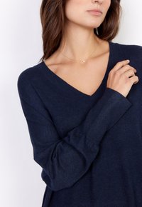 Navyblauer V-Ausschnitt-Pullover aus weichem Strickstoff mit langen Ärmeln. Verfügt über eine lockere Passform und eine dezente Struktur. Goldenes Halskettchen sichtbar.