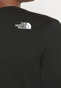 Černé tričko s dlouhým rukávem, které má na horní části zad malé bílé logo "The North Face". Vyrobeno z hladké tkaniny s přiléhavým střihem.