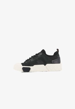 Zwarte sneaker met een gestructureerde bovenkant, vetersluiting, contrasterende witte rubberen zool en patroonaccenten op de zool en hiel.