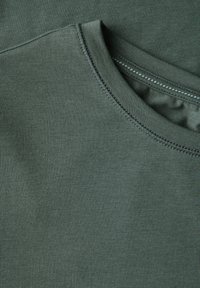 Nærbillede af olivengrøn bomulds-t-shirt stof, med en rund halsudskæring, glat tekstur og sømdetaljer langs kanten.