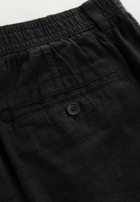 Pantalones cortos de lino negros con cintura elástica y un bolsillo trasero con un solo botón negro. Tejido texturizado y corte relajado.