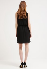 Czarna, bezrękawnikowa sukienka z dopasowanym w pasie fasonem, warstwowym dołem i gładkiego, lekkiego materiału. W połączeniu z czarnymi szpilkami.