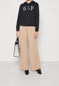 Felpa nera con logo "GAP" in argento, pantaloni larghi beige e una borsa bianca con un accento nero, abbinati a stivali neri a punta.