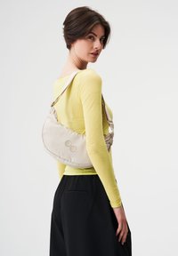 Beige Schultertasche mit geschwungenem Design, gesichert mit einem Riemen. Verfügt über zwei farbige kreisförmige Akzente auf der Vorderseite. Strukturierter Stoff.