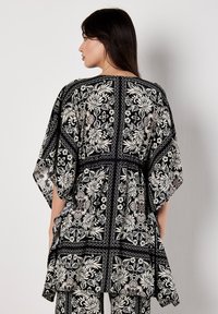 Schwarze Blumenbluse mit weißen und cremfarbenen Mustern, lockere Passform, kurze Ärmel, strukturiertes Material, runder Ausschnitt und seitliche Schlitze.