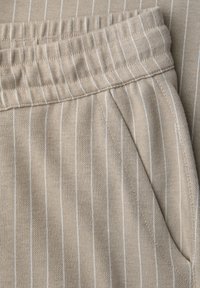 Beiger Stoff mit dünnen weißen vertikalen Nadelstreifen, elastischem Bund und schräger Seitentasche an weich strukturierten Hosen.