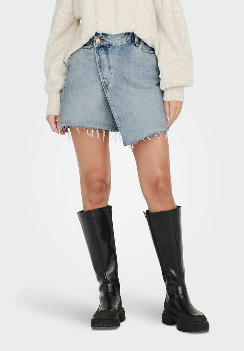 Denim mini krilo ima zbledel svetlo modri odtenek, strgane robove in asimetrično ovijanje. Uporabljeno je z dolgimi črnimi usnjenimi škornji.